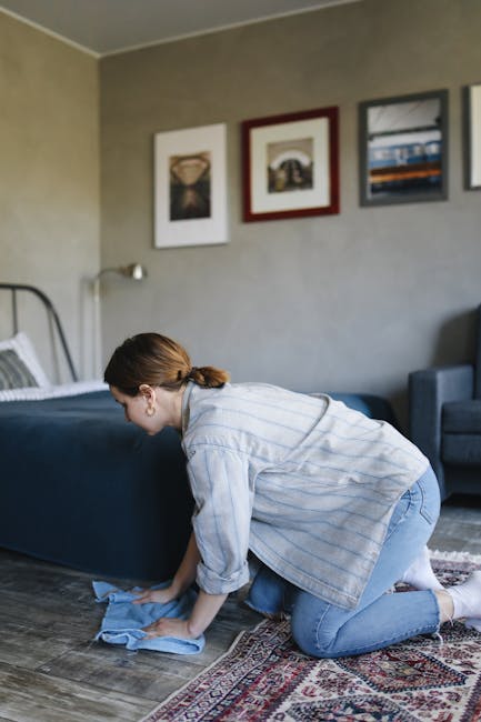 A person is kneeling on a patterned carpet in a room with warm, natural lighting, loading a white cloth into a yellow and black vacuum cleaner placed on the carpet. The vacuum cleaner has a flexible h